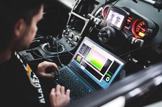 a man sitting in front of a laptop computer on top of a desk next to a car