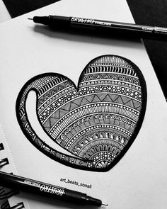 a black and white drawing of a heart with intricate designs on paper next to two markers