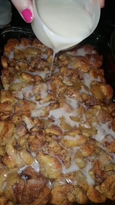 a person pouring milk into a pan filled with cinnamon rolls