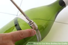 a person is using scissors to cut the bottom of a green bottle with white tiles in the background