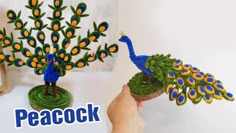 a person holding a fake peacock on top of a table next to a vase with flowers in it