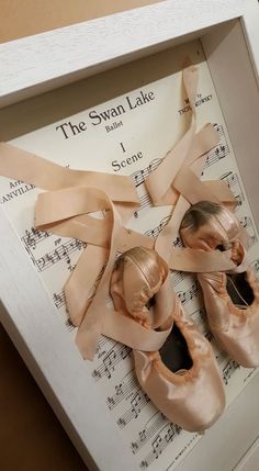 two pairs of ballet shoes are in a box with sheet music behind them and the swan lake logo