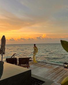 a woman standing on top of a wooden pier next to the ocean