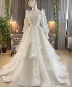 a white wedding dress with long sleeves and ruffled skirt on display in a room