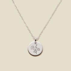 a silver necklace with a small flower on the front and a chain attached to it