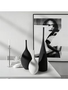 three black and white vases sitting on top of a table next to a candle