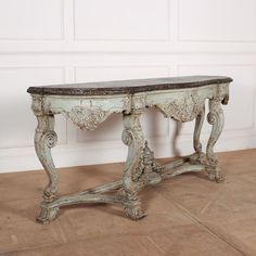 an old wooden table sitting on top of a tile floor next to a white wall