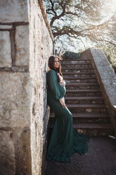 a woman in a green dress leaning against a stone wall