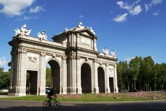 a person riding a bike past a large building with statues on it's sides