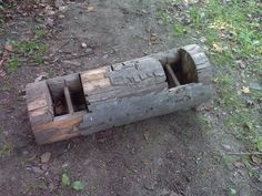 an old wooden boat made out of logs on the ground with grass and trees in the background