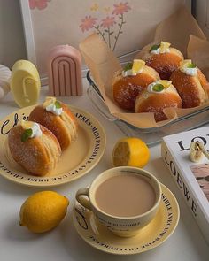 two plates with pastries on them next to a box of lemons and a cup of coffee