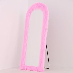 a pink floor mirror sitting on top of a white table next to a black stand