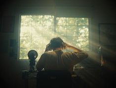 a woman sitting in front of a window with her headphones up to her ears