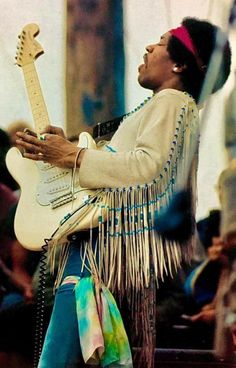 a man holding a guitar in his hands and wearing a headband with fringes on it