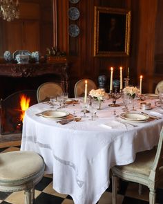 a dining room table set with place settings and candles in front of the fire place