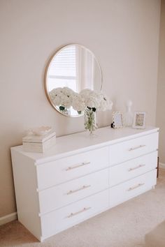 a white dresser topped with flowers and a round mirror