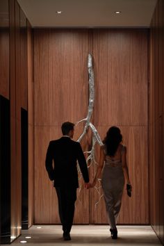 a man and woman walking down a hall holding hands