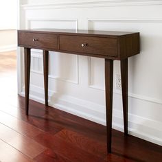 a wooden table sitting on top of a hard wood floor next to a white wall