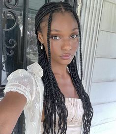 a woman with long braids standing in front of a door wearing a white dress