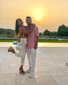 a man and woman standing next to each other in front of a pool at sunset