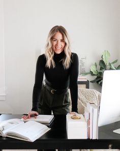 a woman standing in front of a desk with an open book and computer on it