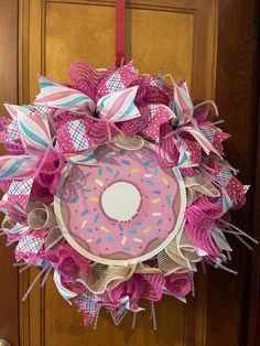 a pink donut wreath hanging on a door with ribbons and bows around it's edges