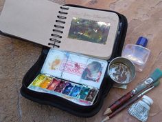 an artist's kit with watercolors, brushes and other art supplies sitting on the ground