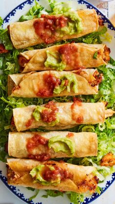 three burritos on a plate with lettuce and tomato sauce in the middle