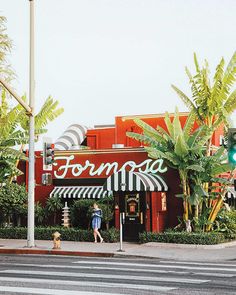 people are walking across the street in front of a food court with palm trees on both sides