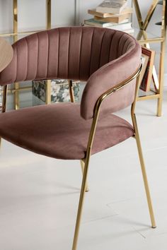 a pink velvet chair with gold legs in front of a bookshelf filled with books