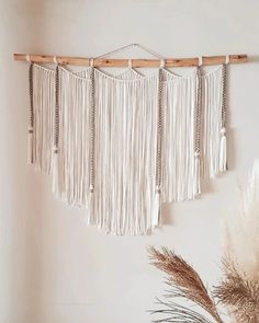 a white wall hanging with several tassels on it next to some dried plants