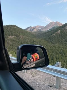 a person taking a photo in the side mirror of a car with mountains in the background