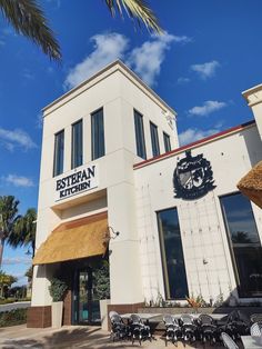 an outside view of a restaurant with tables and chairs on the sidewalk near palm trees