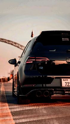 the back end of a black car driving down a road with an arch in the background