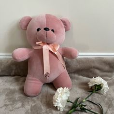 a pink teddy bear sitting next to two white flowers