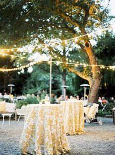 an outdoor dining area with tables covered in yellow tablecloths and lights strung from the trees