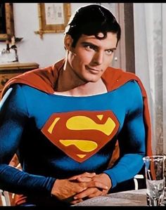 the man in superman costume is sitting at a table with his hands on his chest