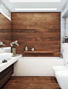 a white bath tub sitting next to a sink under a bathroom mirror with wooden paneling on the wall