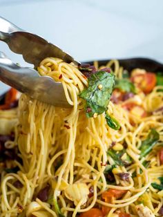 someone using tongs to eat spaghetti with tomatoes and spinach in a skillet