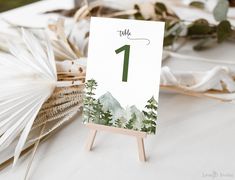 a table number is placed on an easel with pine trees and mountains in the background