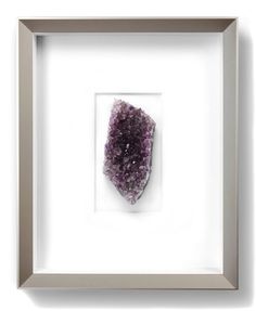 a piece of purple rock in a frame on the wall above it is a white background