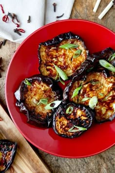 a red plate topped with cooked eggplant on top of a wooden cutting board