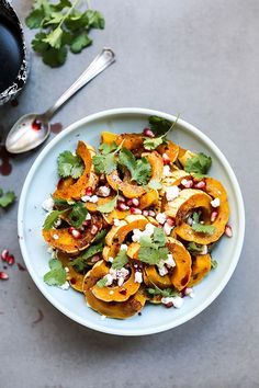 a white plate topped with squash and pomegranates next to a glass of wine