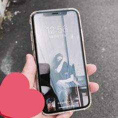 a person holding an iphone in their hand with a red heart on the ground next to them