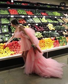 a woman in a pink dress is walking through a produce section