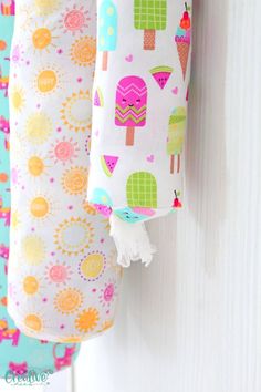 three colorful items hanging from hooks on a white wall with flowers and ice creams