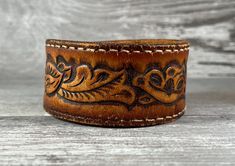 This distressed brown genuine leather cuff, beautifully crafted from an upcycled belt, features a beautiful hand tooled floral detail for a cool western, rock star, boho, rustic, or biker style. See close-up shots for the wonderful distressing that adds to the character of this handmade beauty.  Like all genuine leather goods, the cuff will continue to soften and become more pliable with every wear. Also, I use quality heavy-duty snaps which will seem tight at first, but will loosen a bit with wear. SIZING: The bracelet has two snaps for an adjustable fit, and should comfortably fit up to a 7" wrist. Not sure what size your wrist is? Check out this free printable tape measure by cutting and pasting this link into your browser: https://www.inchcalculator.com/printable-tape-measure/ It is my Bracelet For Him, Leather Cuff Bracelet, Handmade Beauty Products, Rustic Boho, Leather Cuffs Bracelet, Recycled Leather, Biker Style, Leather Cuffs, Rock Star