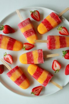 four popsicles on a plate with strawberries and oranges next to each other