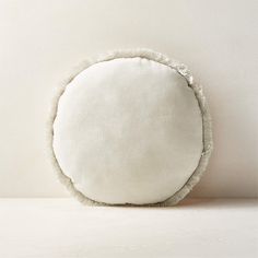 a white round pillow with ruffled edges sitting on a countertop next to a wall