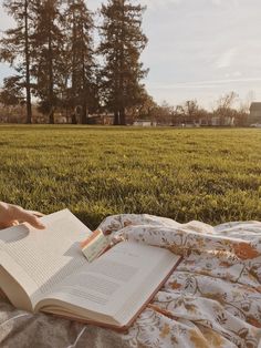 a person laying on a blanket reading a book in the middle of a grassy field